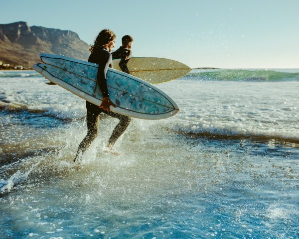 Two male surfers going for surfing in the sea. Two men carrying surfboards running in to the sea for surfing.